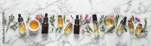 Flat lay composition with bottles of natural tea tree oil and space for text on white marble background