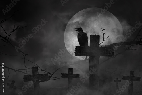 Scary background the black crow perched on cemetery cross in fog dark and light with dark silhouette in large moon and abandoned large cities, concept of horror and Halloween