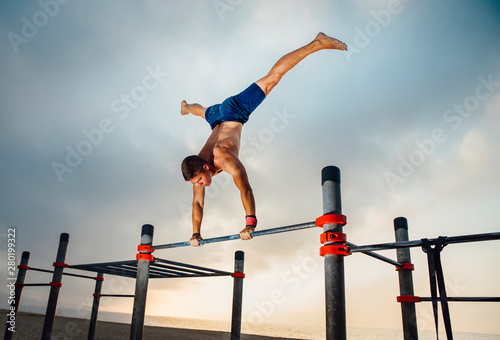 fitness, sport, training, calisthenics and lifestyle concept - young man exercising handstand on bar outdoors