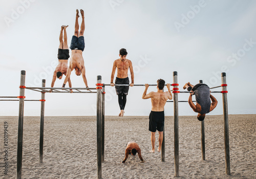 fitness, sport, training, calisthenics and lifestyle concept - Group of guys training on the beach workout bars