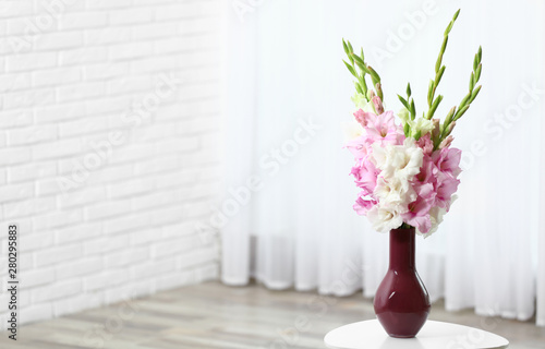Vase with beautiful gladiolus flowers on wooden table indoors. Space for text