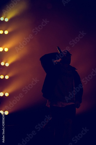 Silhouette of young rap singer with microphone in hand. Cool hip hop arists performing live on stage. Backlit photo of rapper singing on musica festival scene