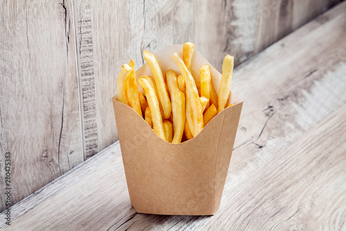 Close up view on Potatoes French Fries in Carton Package Box Isolated on wooden background. Fast food concept mock up. Blank kraft or craft paper cardboard with french fries fry