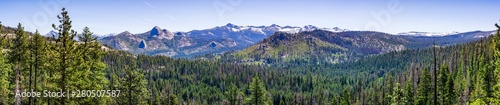 Panoramic view of wilderness areas in Yosemite National Park with evergreen forests covering valleys and snow capped mountains visible in the background; Sierra Nevada mountains, California