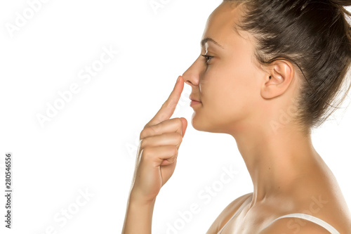 young woman touches her nose with her finger on a white background
