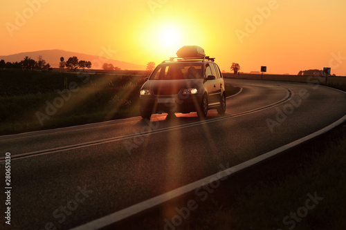Samochód z bagażnikiem dachowym na zakręcie drogi o zachodzie słońca.