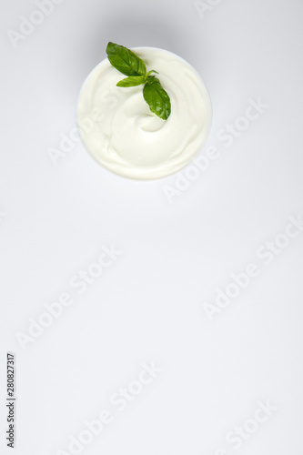 Bowl of fresh sour cream with basil on white background, top view
