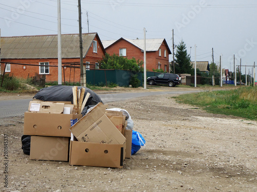 Black plastic bags of garbage and cardboard boxes with folded cardboard lie along the road. Garbage collection in the village.