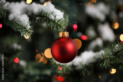 Traditional artificial Christmas tree with red ball ornament with glowing lights and snow in background