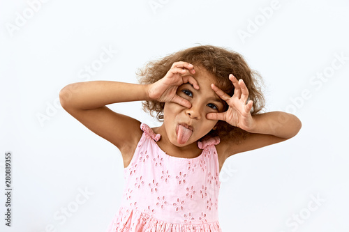 Making face,funny foolishes portrait of little African American girl, against white background.