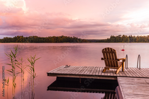 Wooden lounge chairs at Sunset on a pier on the shores of the calm Saimaa lake in Finland under a nordic sky on fire - 1