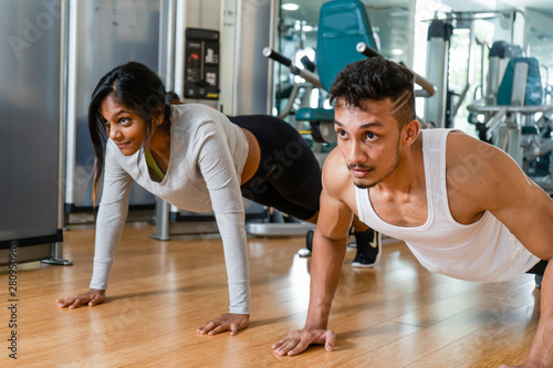 Cheerful young couple exercising forearm plank side by side on mats during workout in the interior of a modern fitness club