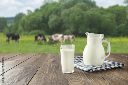 Fresh milk in glass on dark wooden table and blurred landscape with cow on meadow. Healthy eating. Rustic style.