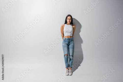 full length view of beautiful girl standing near wall and looking at camera