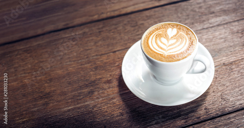 Zamyka w górę gorącej cappuccino białej filiżanki z kierową kształta latte sztuką na ciemnego brązu starego drewna stole przy kawiarni, jedzenia i napoju pojęciem ,.
