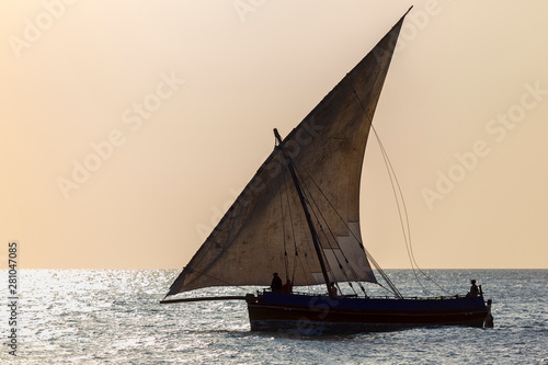 traditional dhow sailing boat silhouetted against a warm sky and shimmering ocean