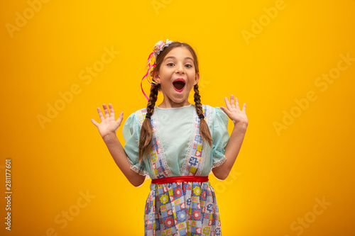 Child in typical clothes of famous Brazilian party called "Festa Junina" in celebration of São João. Beautiful girl on yellow background.