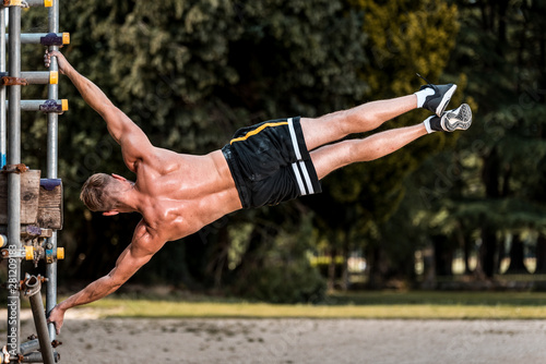 Fit Muscular man performing calisthenics fitness workout on outdoor scaffolding