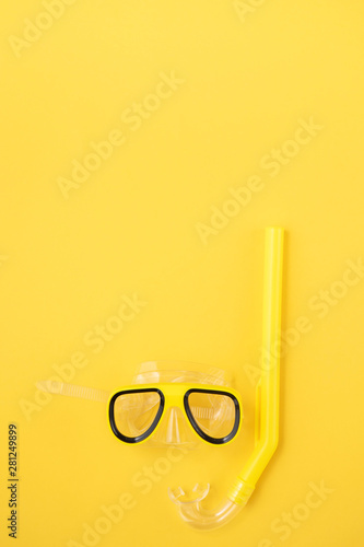 A yellow snorkel and diving mask on a yellow background. overhead lay flat