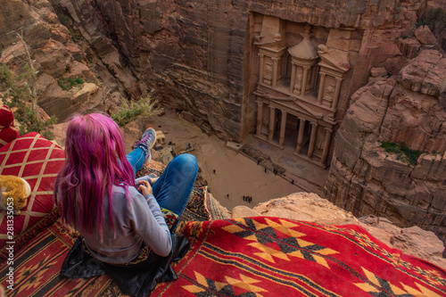 top view travel photography of touristic girl with pink hair sit on edge of cliff back to camera and looking on Petra treasure ancient architecture Jordan national heritage site 