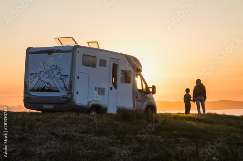 mother and son watching the sunset with their motor home at the edge of the sea