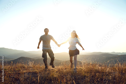 A young couple holding hands and having fun. Dawn in the mountains, the beginning of a new day
