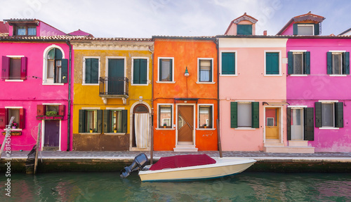 bright colored picturesque buildings near a chanel with boat , houses of Burano in the evening