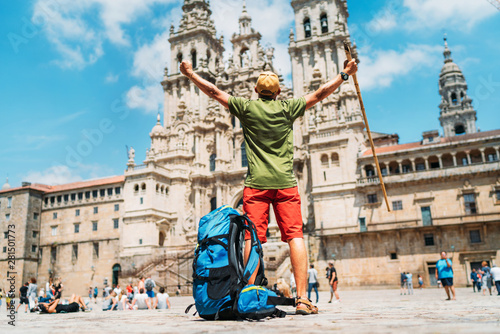 Young backpacker man pilgrim standing with raised arms on the Obradeiro square (plaza) - the main square in Santiago de Compostela as a end of his Camino de Santiago pilgrimage.