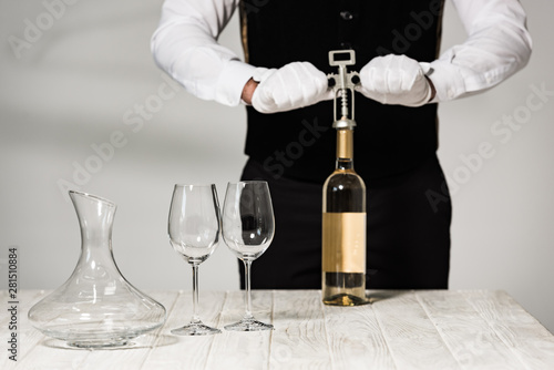 partial view of waiter in white gloves opening bottle of wine with corkscrew