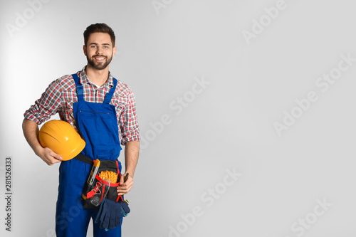 Portrait of construction worker with tool belt on light background. Space for text