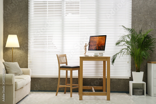 Comfortable workplace near window with blinds in room
