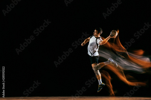 Caucasian young handball player in action and motion in mixed lights over black studio background. Fit male professional sportsman. Concept of sport, movement, energy, dynamic, healthy lifestyle.