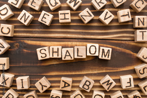 Shalom - word from wooden blocks with letters, Jewish greeting or saying goodbye concept, random letters around, top view on wooden background