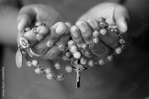 Rosary in hand in black and white. Young junior lady holding rosary with open hand with Jesus Christ Cross Crucifix. Month of Rosary, Christian Catholic religious symbol of faith concept.