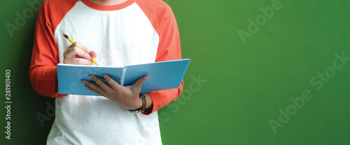 High school, university student in casual writing on paper notebook, Teenager student writing notebook standing in fornt of green wall with copy space at school campus, College education