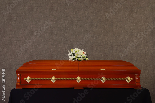 Wooden funeral casket with white lilies at grey wall