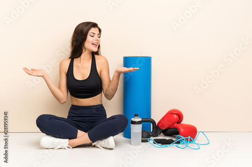 Teenager sport girl sitting on the floor holding copyspace with two hands