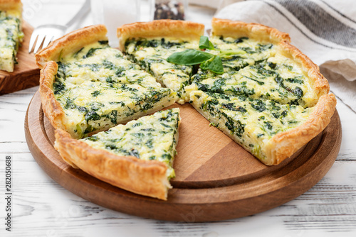 Vegetarian spinach pie or tart with feta cheese on white wooden background.