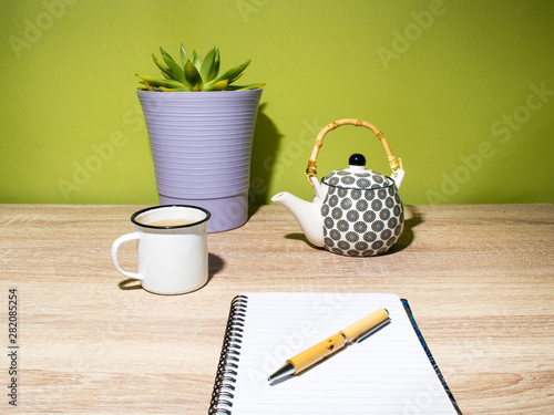 Close-up of moment of relaxation and creativity with a tea and blank paper - bamboo and ceramic teapot, bamboo pen and crass plant 