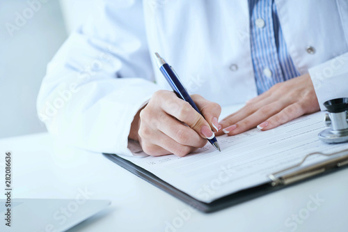 Female medicine doctor hand holding silver pen writing something on clipboard closeup.. Ward round, patient visit check, medical calculation and statistics concept.