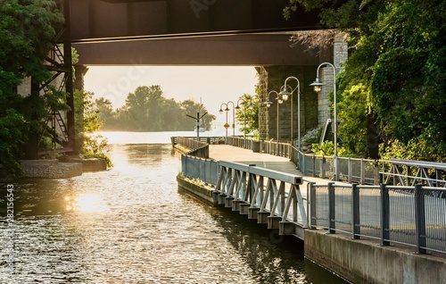 A walkway going along water canal and under the highway overpass