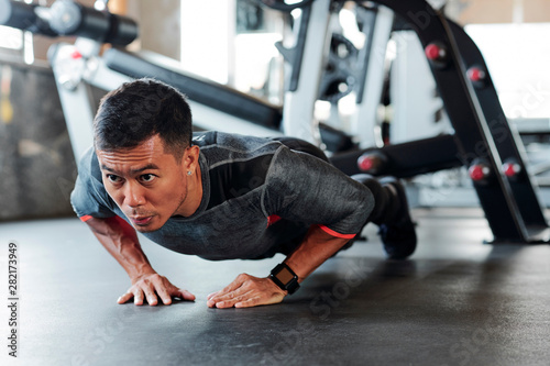 Strong fit young Asian man doing diamond push-ups in gym during sports training