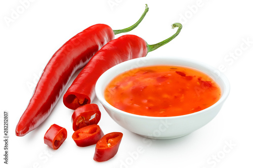 Sweet chilli sauce in a white ceramic bowl next to one whole and one cut red chilli isolated on white.