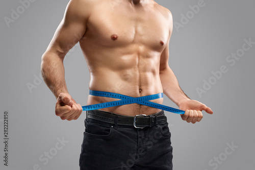 Crop slim guy measuring waistline