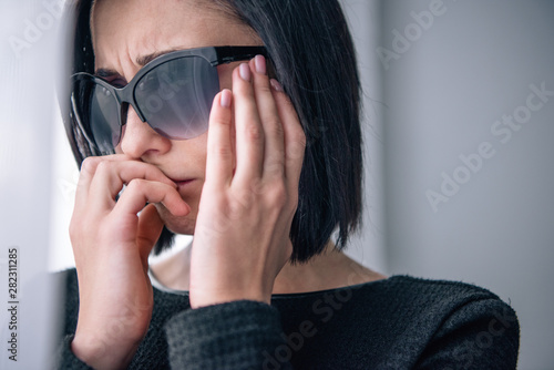 depressed woman in sunglasses covering mouth and grieving at home