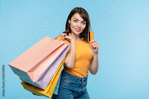 Happy young shopaholic with several paperbags boasting with credit card