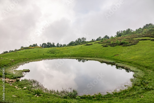 View of a mountain lake with clear water and reflection at cloudy summer day.