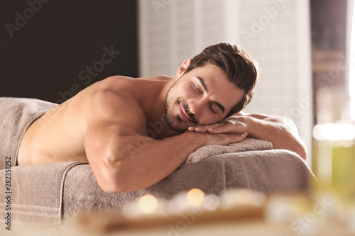 Handsome young man relaxing on massage table in spa salon