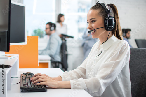 Friendly customer support operator with headset and microphone assisting to client in call centre