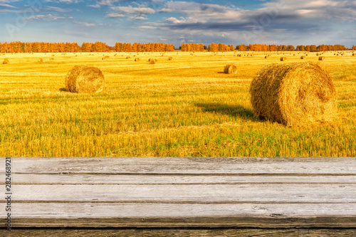 Empty wooden table with blurred autumn landscape of beveled field and straw bales. Mock up for display or montage products